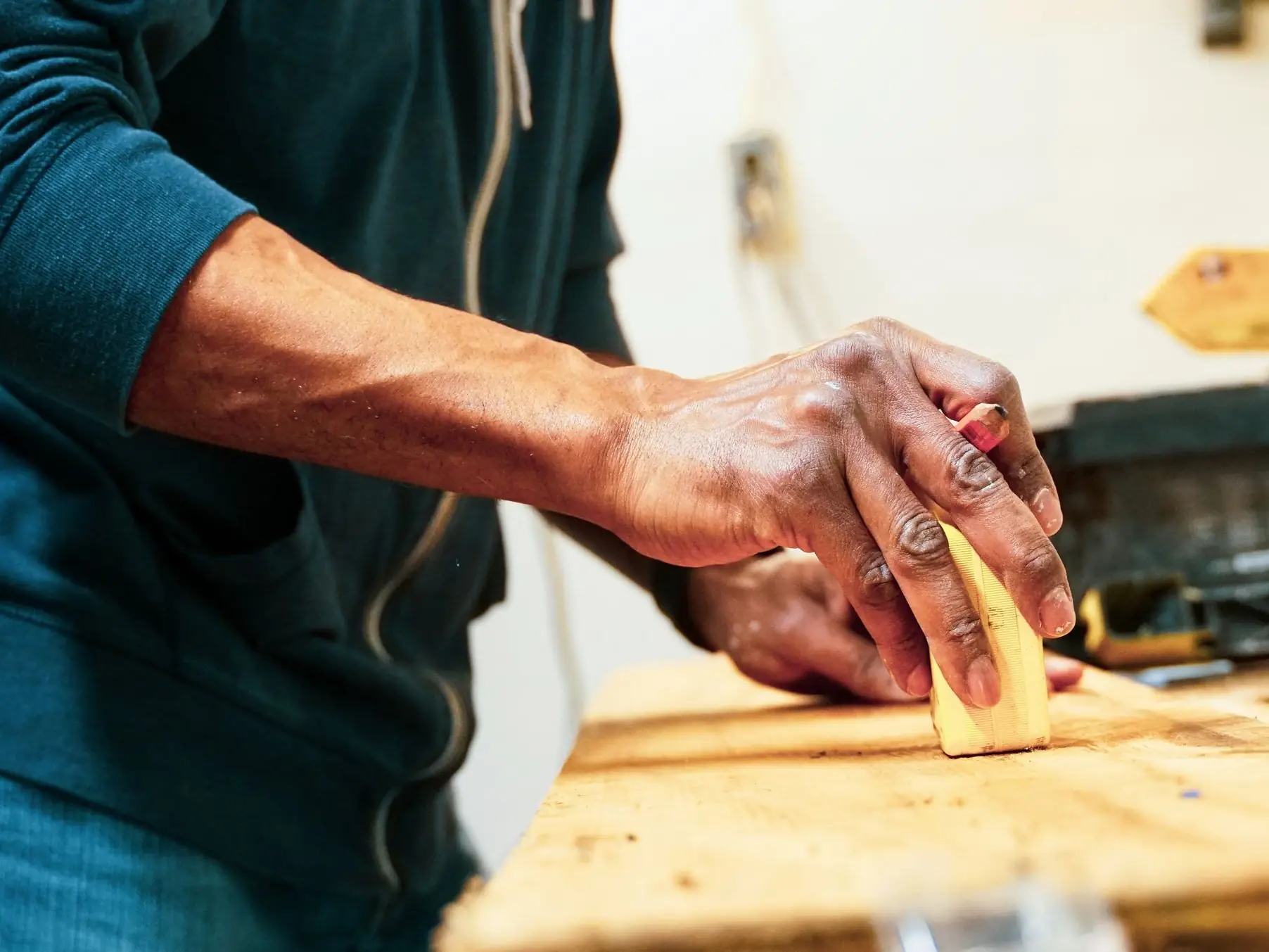 Iemand schuurt een houten plank op een werkbank.